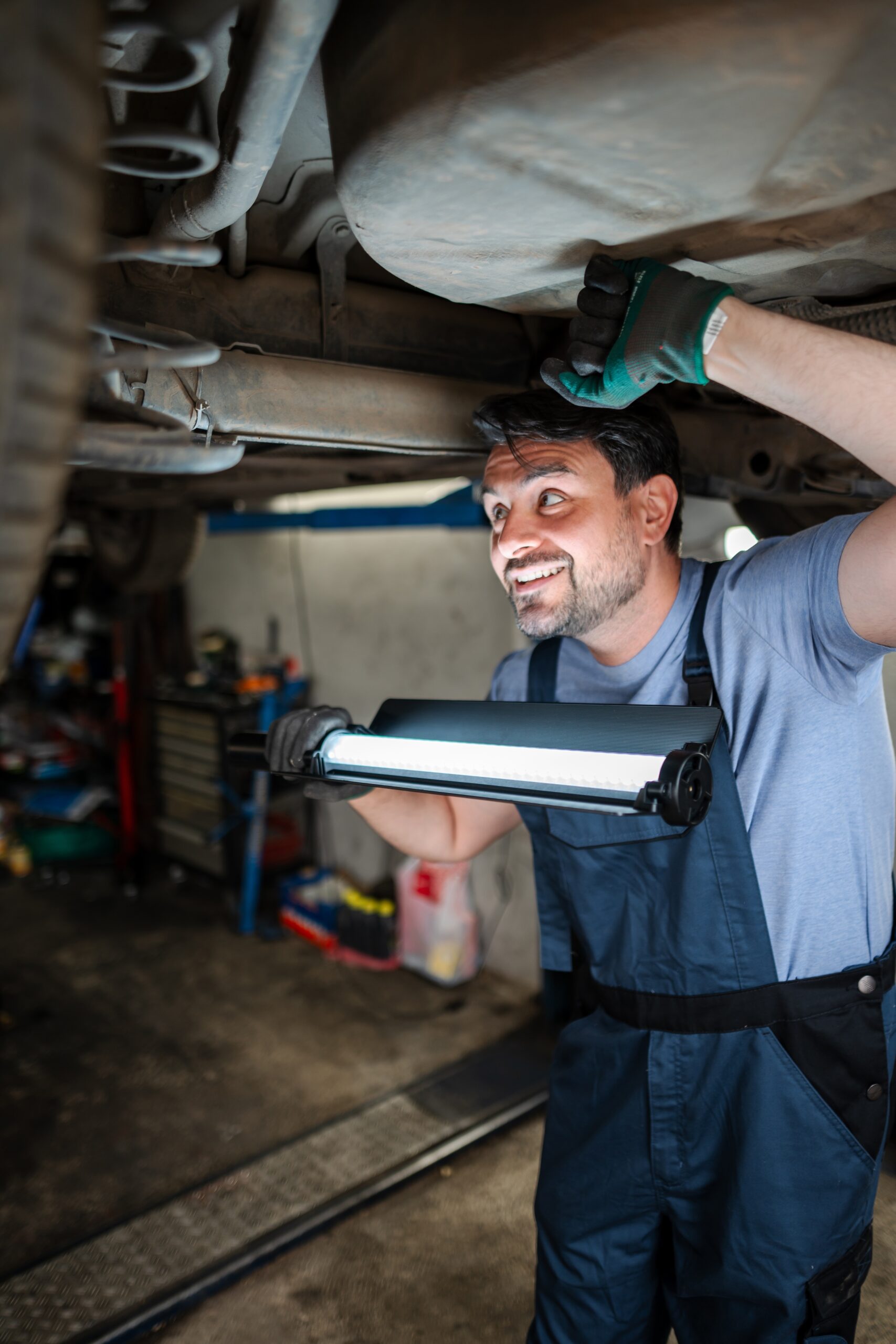 Car mechanic inspecting vehicle undercarriage with work light