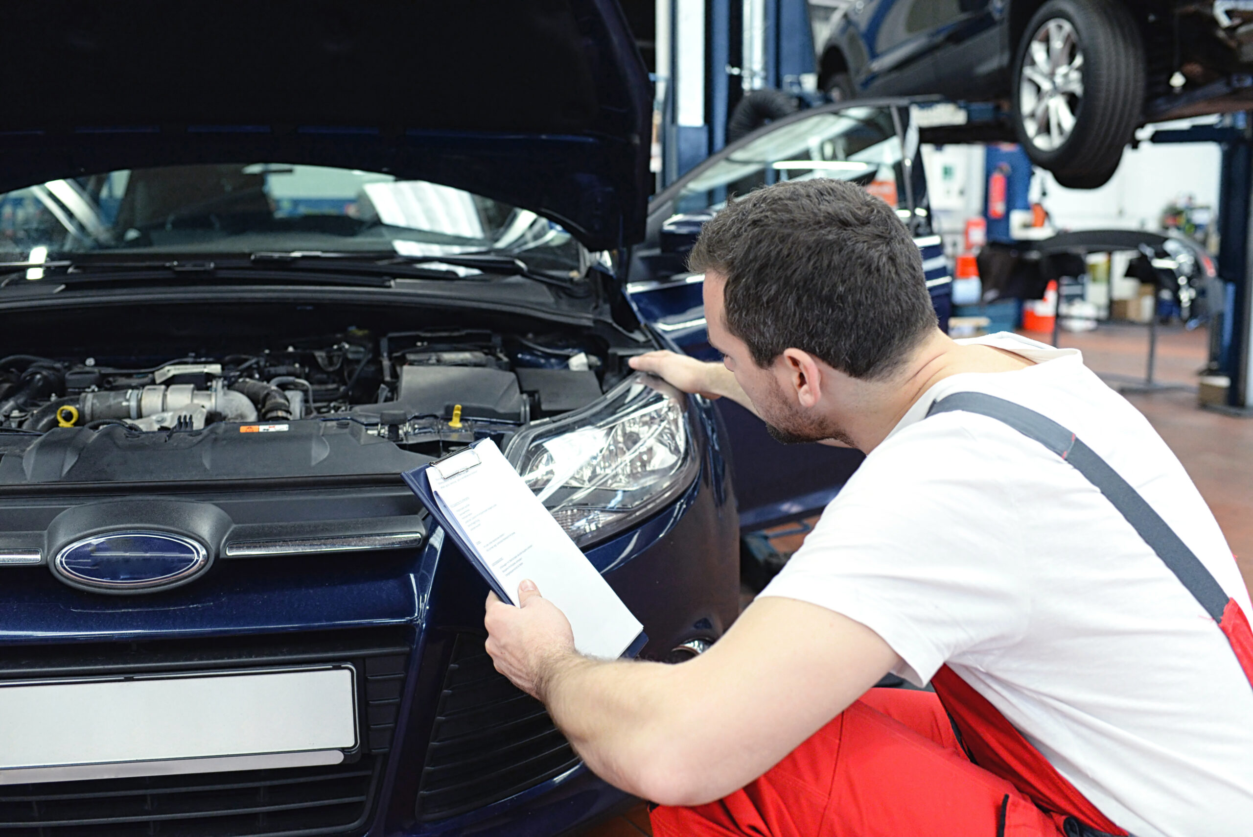 Automechaniker kontrolliert Scheinwerfer – Lichtanlage beim KFZ in der Werkstatt // Car mechanic checks headlights – lighting system in the workshop of a motor vehicle